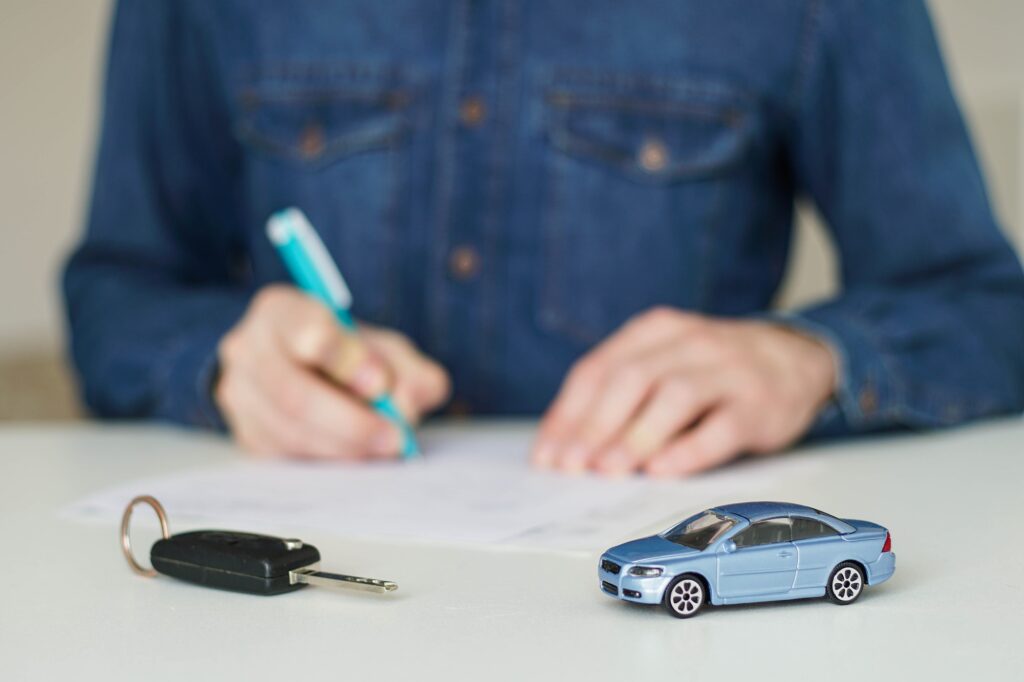 Young man signing car insurance documents on the background.